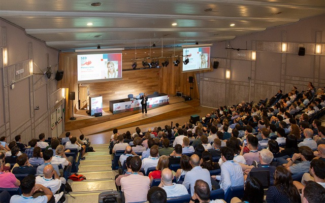 An auditorium full of people watches a plenary talk